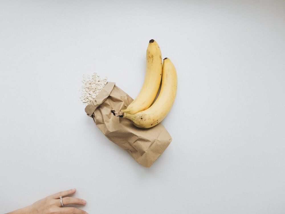 raw oats in a brown paper bag with two ripe bananas