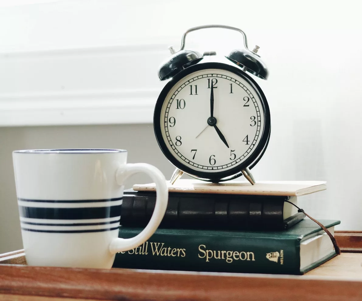 Trust God's Perfect Timing. Photo of a clock on some books alongside a cup of coffee